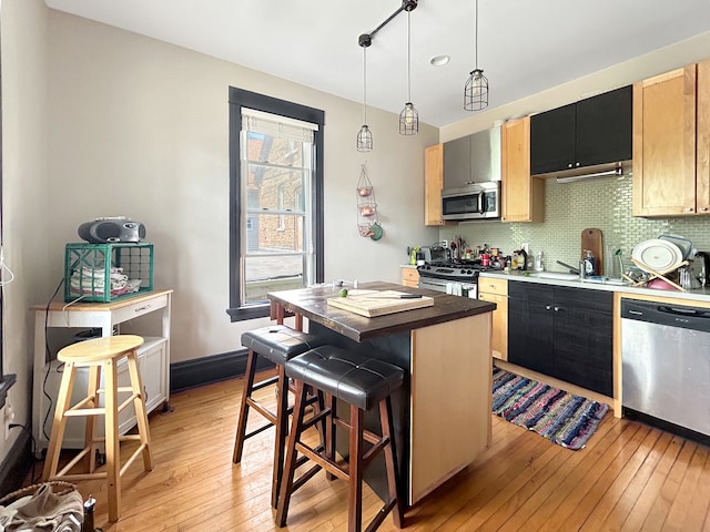 kitchen with decorative backsplash, appliances with stainless steel finishes, decorative light fixtures, light wood-type flooring, and a kitchen island