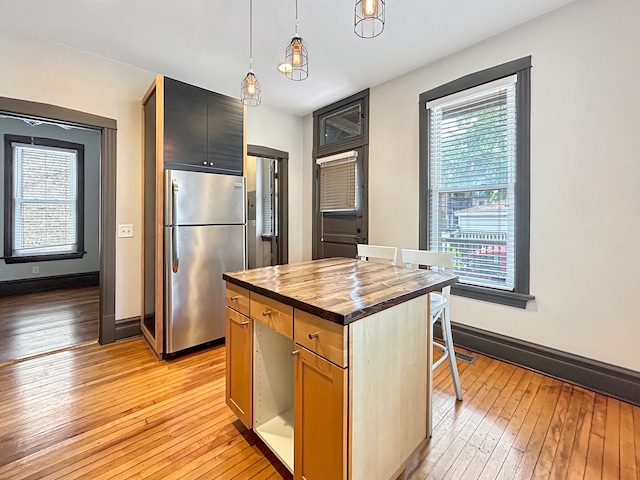 kitchen featuring stainless steel refrigerator, wooden counters, a center island, decorative light fixtures, and light wood-type flooring