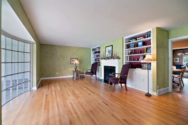 sitting room with built in shelves, light hardwood / wood-style flooring, and a chandelier