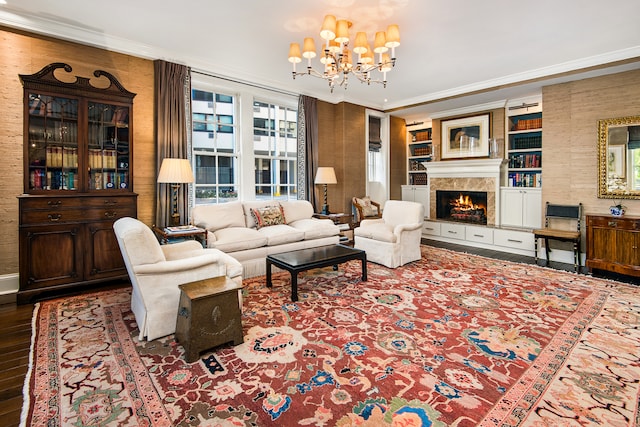 living room featuring built in features, hardwood / wood-style floors, an inviting chandelier, a fireplace, and ornamental molding