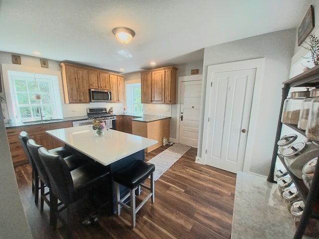 kitchen with a kitchen island, backsplash, dark wood-type flooring, appliances with stainless steel finishes, and a kitchen bar