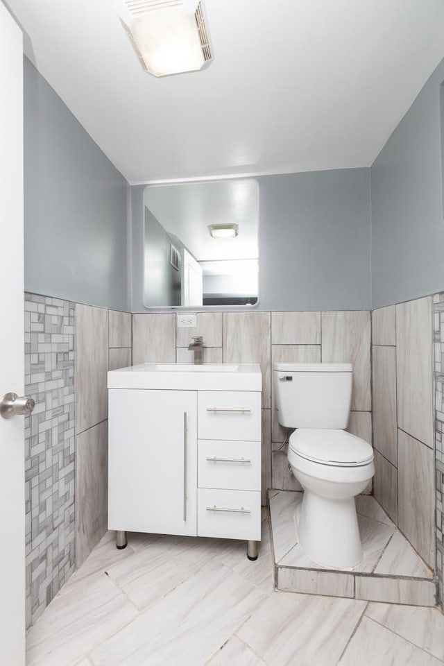 bathroom featuring tile walls, toilet, wainscoting, and vanity