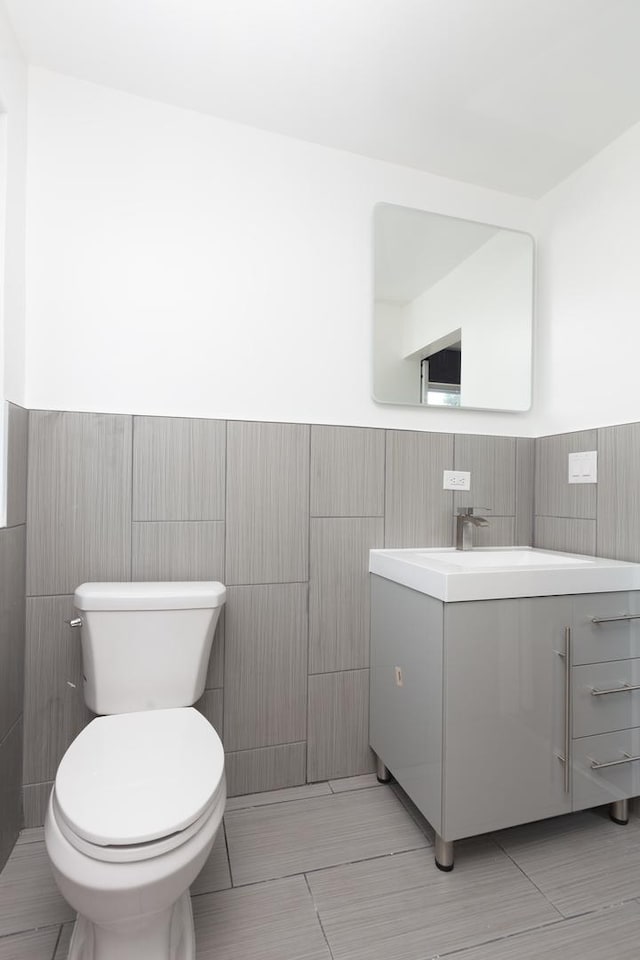 bathroom with tile walls, toilet, vanity, wainscoting, and tile patterned flooring