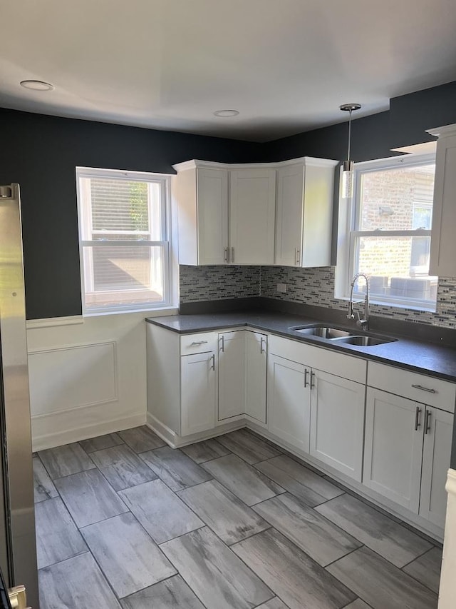 kitchen featuring a sink, white cabinets, dark countertops, decorative backsplash, and decorative light fixtures