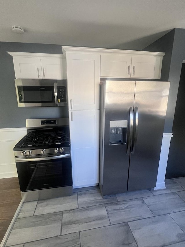 kitchen with appliances with stainless steel finishes, white cabinetry, and wainscoting