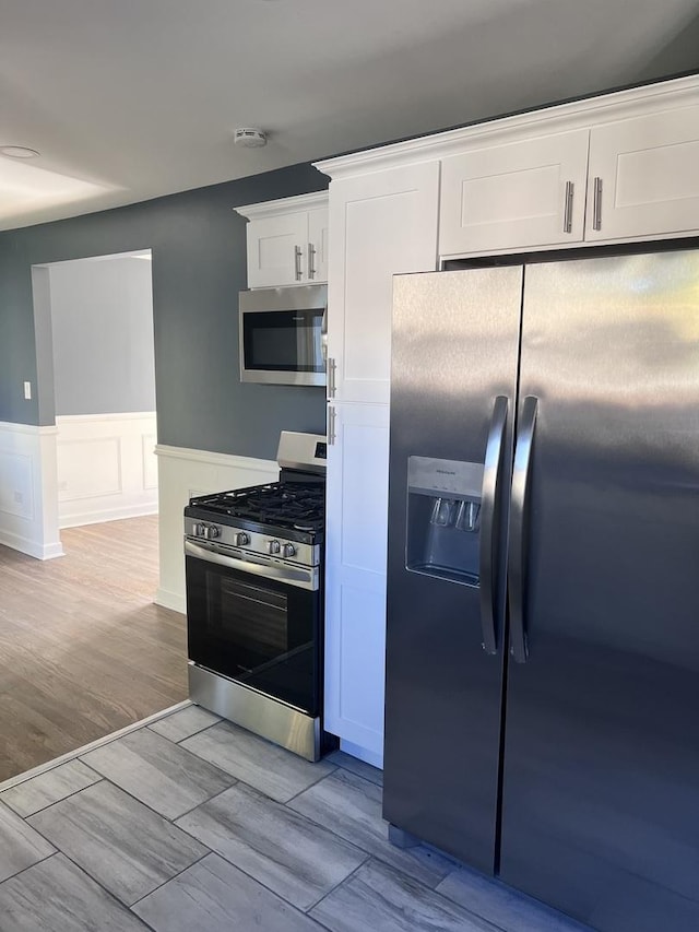 kitchen with stainless steel appliances, wainscoting, white cabinets, and light wood-style flooring