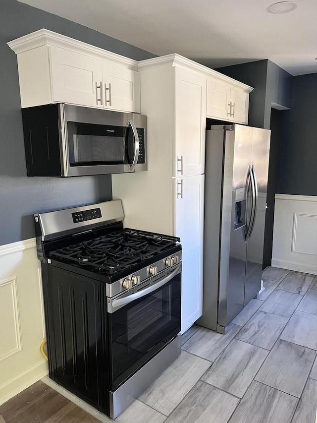 kitchen featuring appliances with stainless steel finishes, light wood finished floors, a wainscoted wall, white cabinetry, and a decorative wall
