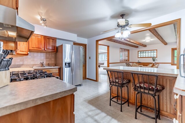 kitchen featuring tasteful backsplash, stainless steel fridge, a breakfast bar, wall chimney range hood, and ceiling fan