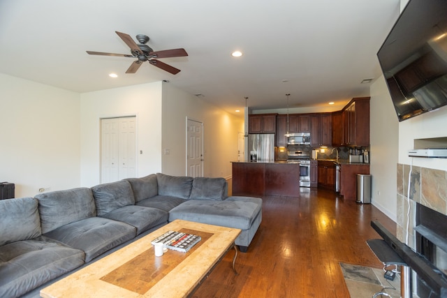 living room featuring ceiling fan, a fireplace, sink, and dark hardwood / wood-style floors