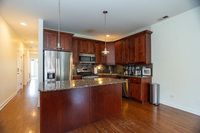 kitchen with appliances with stainless steel finishes, a center island, wood-type flooring, and backsplash