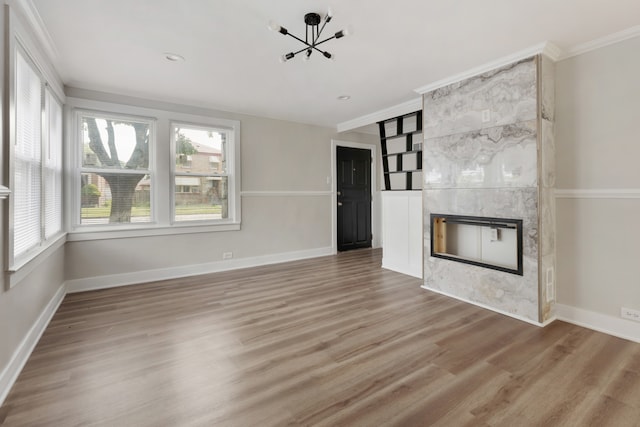 unfurnished living room with hardwood / wood-style flooring, crown molding, a fireplace, and an inviting chandelier