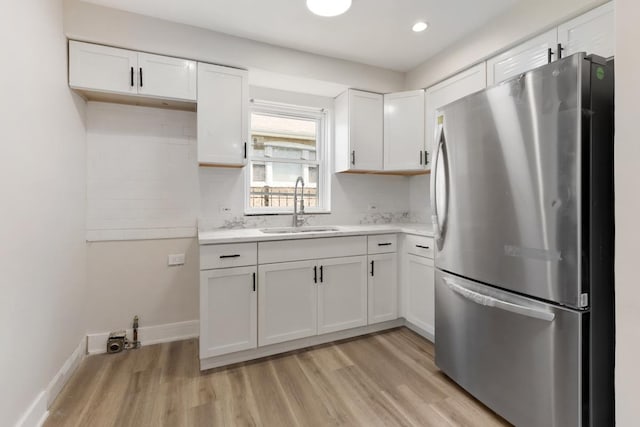 kitchen featuring stainless steel refrigerator, sink, and white cabinets