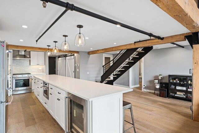 kitchen with wall chimney exhaust hood, beverage cooler, light hardwood / wood-style floors, stainless steel appliances, and white cabinetry