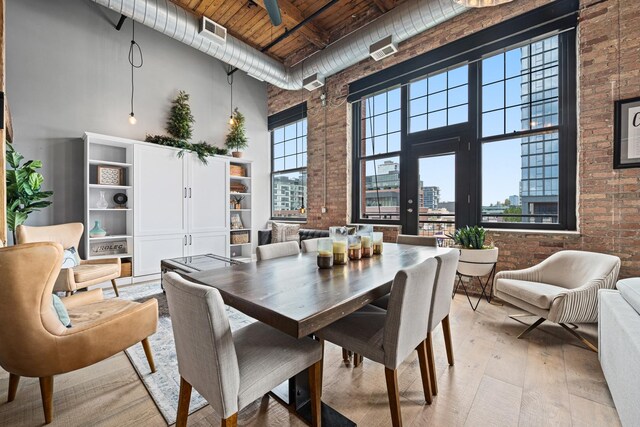 dining area featuring light hardwood / wood-style flooring, wood ceiling, brick wall, and a towering ceiling