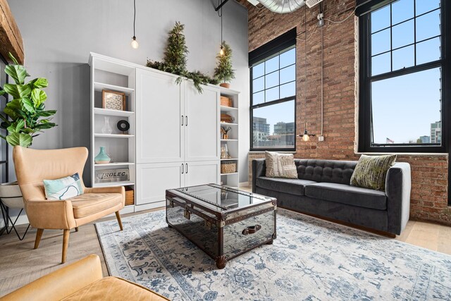 living room featuring a towering ceiling, brick wall, and light hardwood / wood-style floors