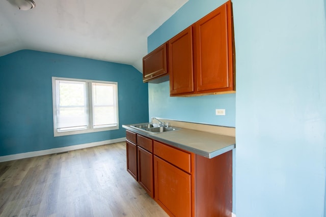 kitchen with a sink, baseboards, vaulted ceiling, light wood-style floors, and brown cabinetry