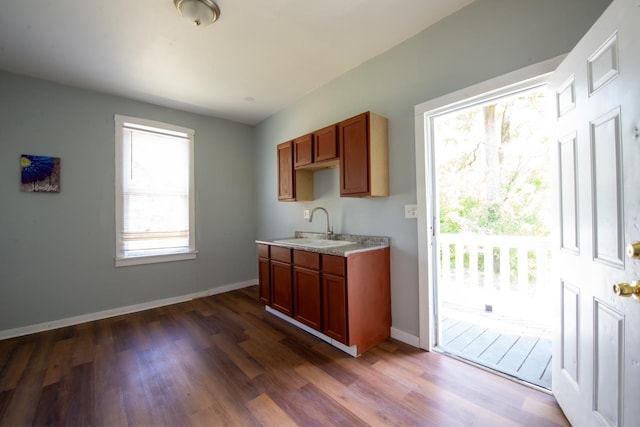 kitchen with baseboards, brown cabinetry, dark wood-style floors, light countertops, and a sink