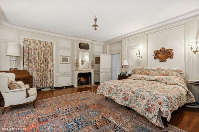 bedroom with a decorative wall, ornamental molding, wood finished floors, and a fireplace with flush hearth