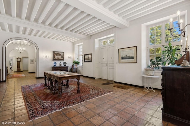 entrance foyer with beam ceiling, baseboards, arched walkways, and an inviting chandelier