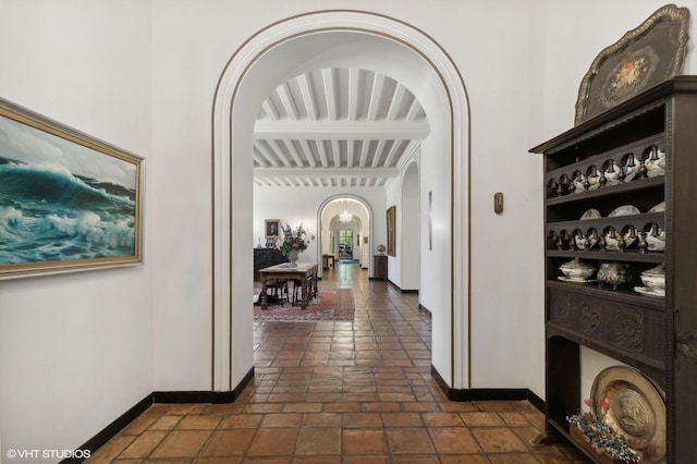 corridor with arched walkways, baseboards, and beamed ceiling