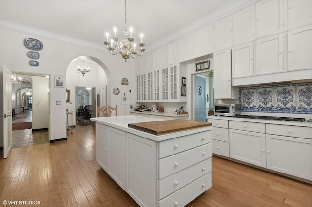 kitchen featuring a notable chandelier, a center island, gas cooktop, arched walkways, and light wood finished floors
