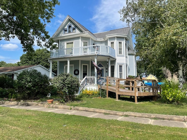 victorian-style house with a balcony, a porch, and a front lawn