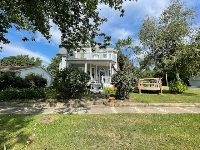 victorian-style house featuring a front lawn, covered porch, and a balcony