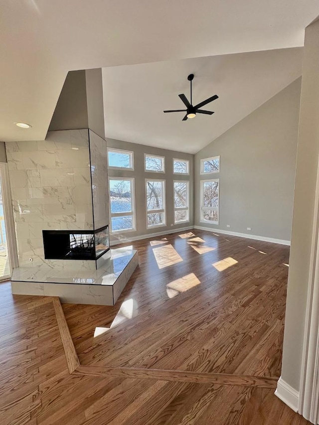 unfurnished living room featuring ceiling fan, high vaulted ceiling, a multi sided fireplace, and hardwood / wood-style flooring