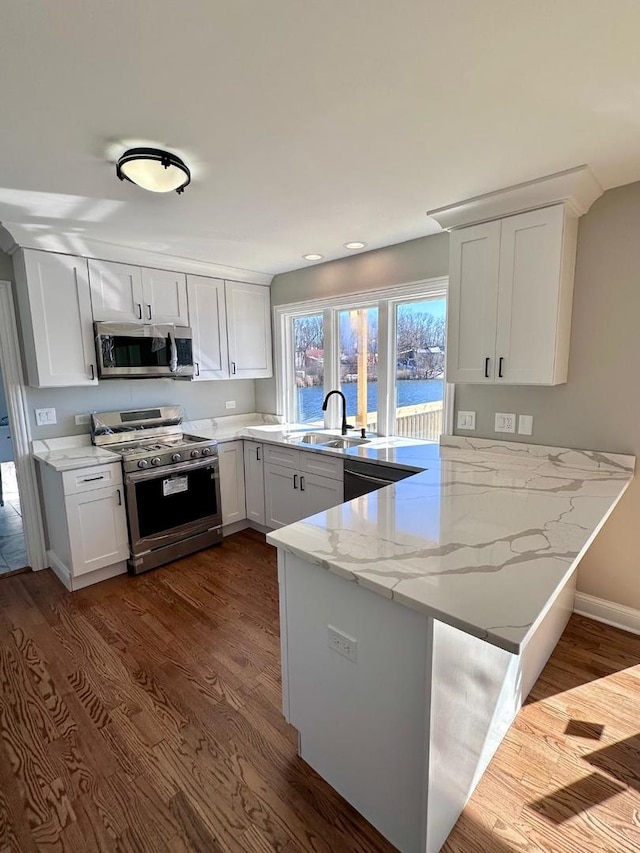 kitchen with hardwood / wood-style floors, kitchen peninsula, white cabinetry, gas range, and light stone counters