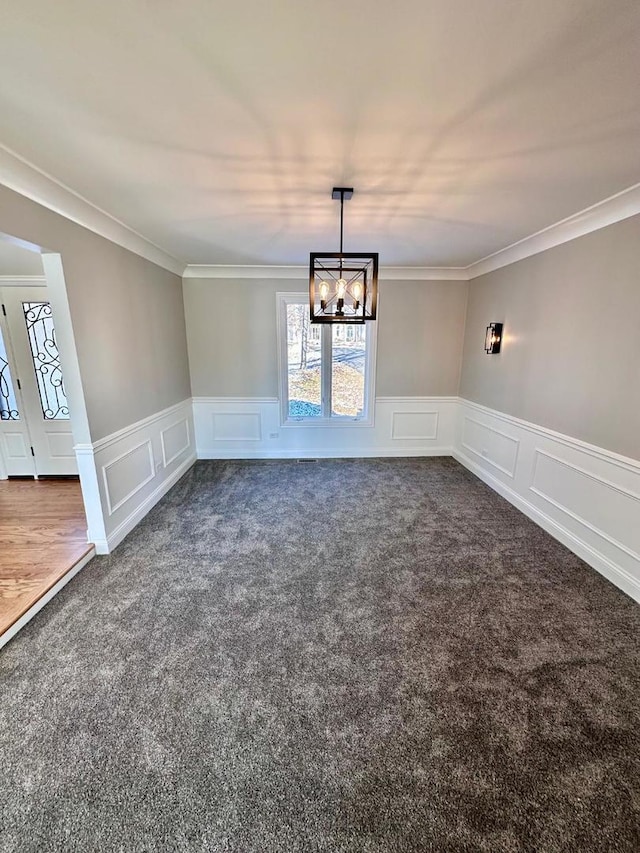 unfurnished room with ornamental molding, dark colored carpet, and an inviting chandelier