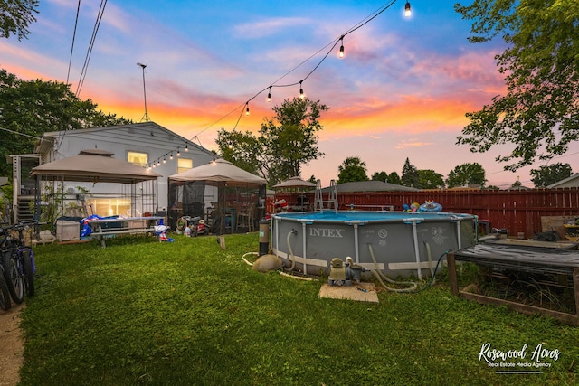 pool at dusk featuring a gazebo and a yard