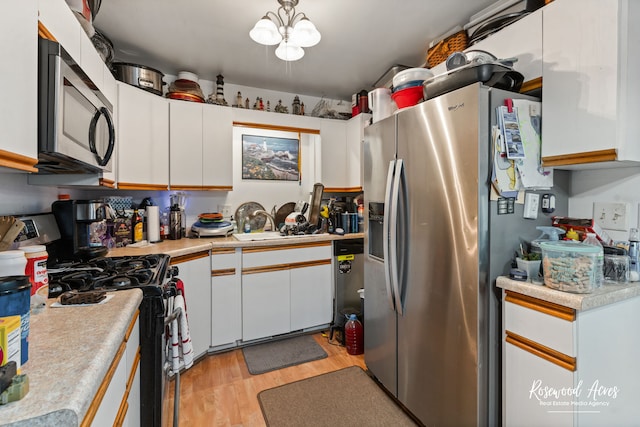 kitchen featuring pendant lighting, stainless steel appliances, white cabinetry, light hardwood / wood-style flooring, and sink