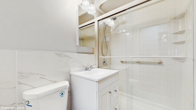 bathroom featuring vanity, toilet, a shower with door, and tile walls