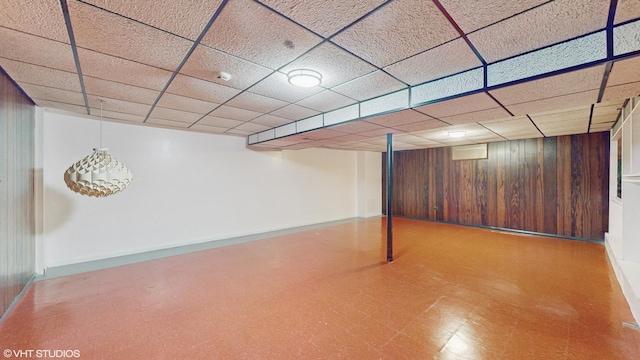 basement featuring a paneled ceiling and wood walls