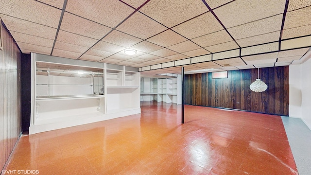 basement featuring a drop ceiling and wood walls