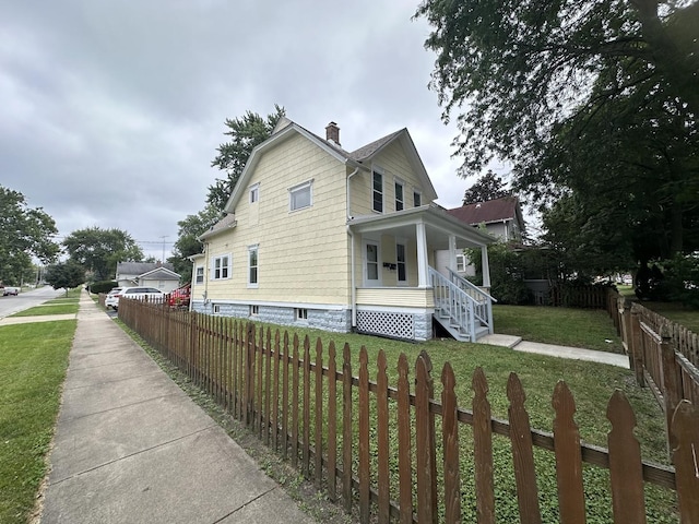 view of property exterior featuring a yard, covered porch, a fenced front yard, and a chimney