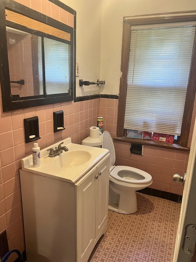 half bath featuring toilet, tile walls, wainscoting, tile patterned flooring, and vanity