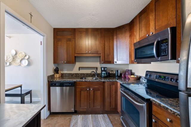 kitchen featuring a textured ceiling, stainless steel appliances, dark stone counters, light tile patterned floors, and sink