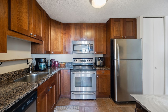 kitchen featuring dark stone counters, a textured ceiling, stainless steel appliances, and sink