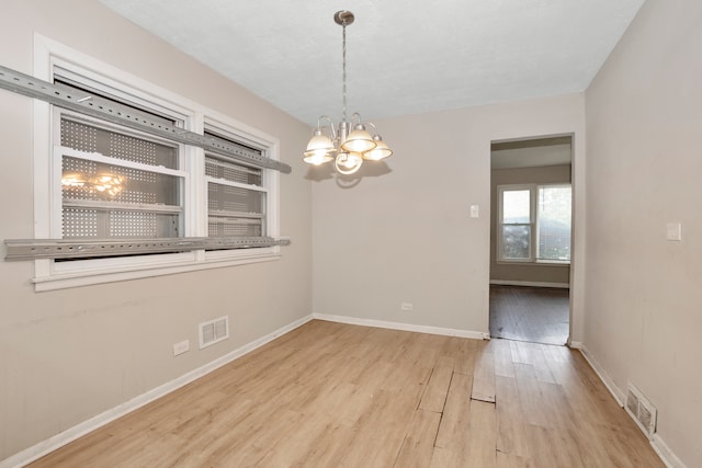 spare room featuring light wood-type flooring and an inviting chandelier