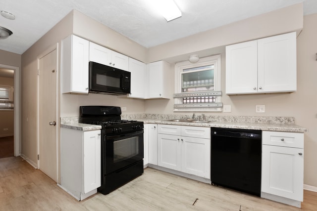 kitchen with white cabinetry, a textured ceiling, black appliances, sink, and light hardwood / wood-style floors