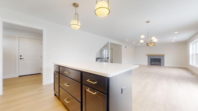 kitchen featuring light wood-type flooring, a center island, a brick fireplace, and hanging light fixtures