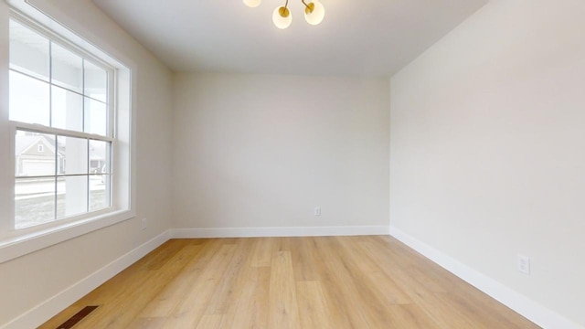 empty room with a notable chandelier and light wood-type flooring