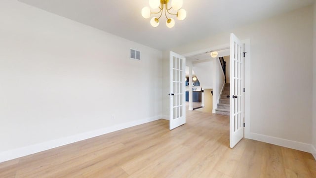 spare room featuring french doors, light wood-type flooring, and an inviting chandelier