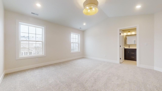 unfurnished bedroom with ensuite bathroom, light colored carpet, and vaulted ceiling