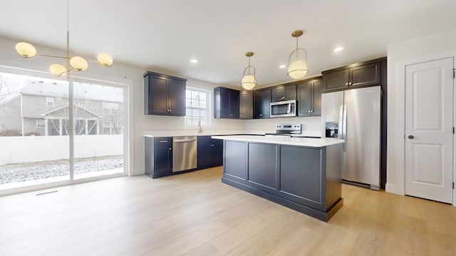 kitchen featuring a center island, light wood-type flooring, stainless steel appliances, and hanging light fixtures