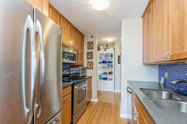 kitchen featuring light hardwood / wood-style flooring, tasteful backsplash, a textured ceiling, stainless steel appliances, and sink