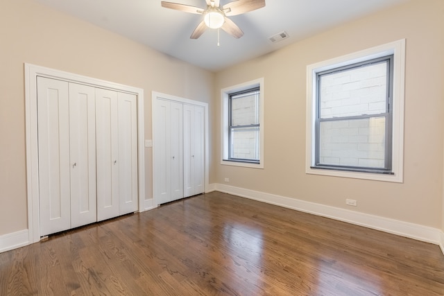 unfurnished bedroom featuring ceiling fan, dark hardwood / wood-style flooring, and two closets