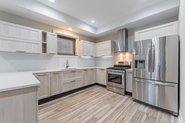 kitchen with appliances with stainless steel finishes, tasteful backsplash, wall chimney range hood, sink, and light brown cabinets