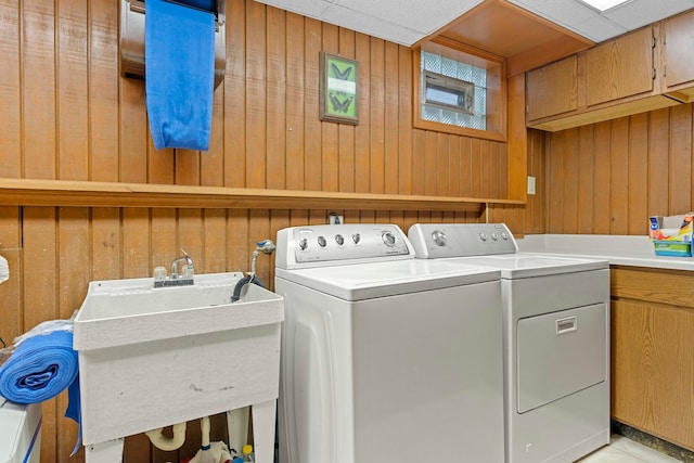 laundry area featuring cabinets, wood walls, washer and clothes dryer, and sink